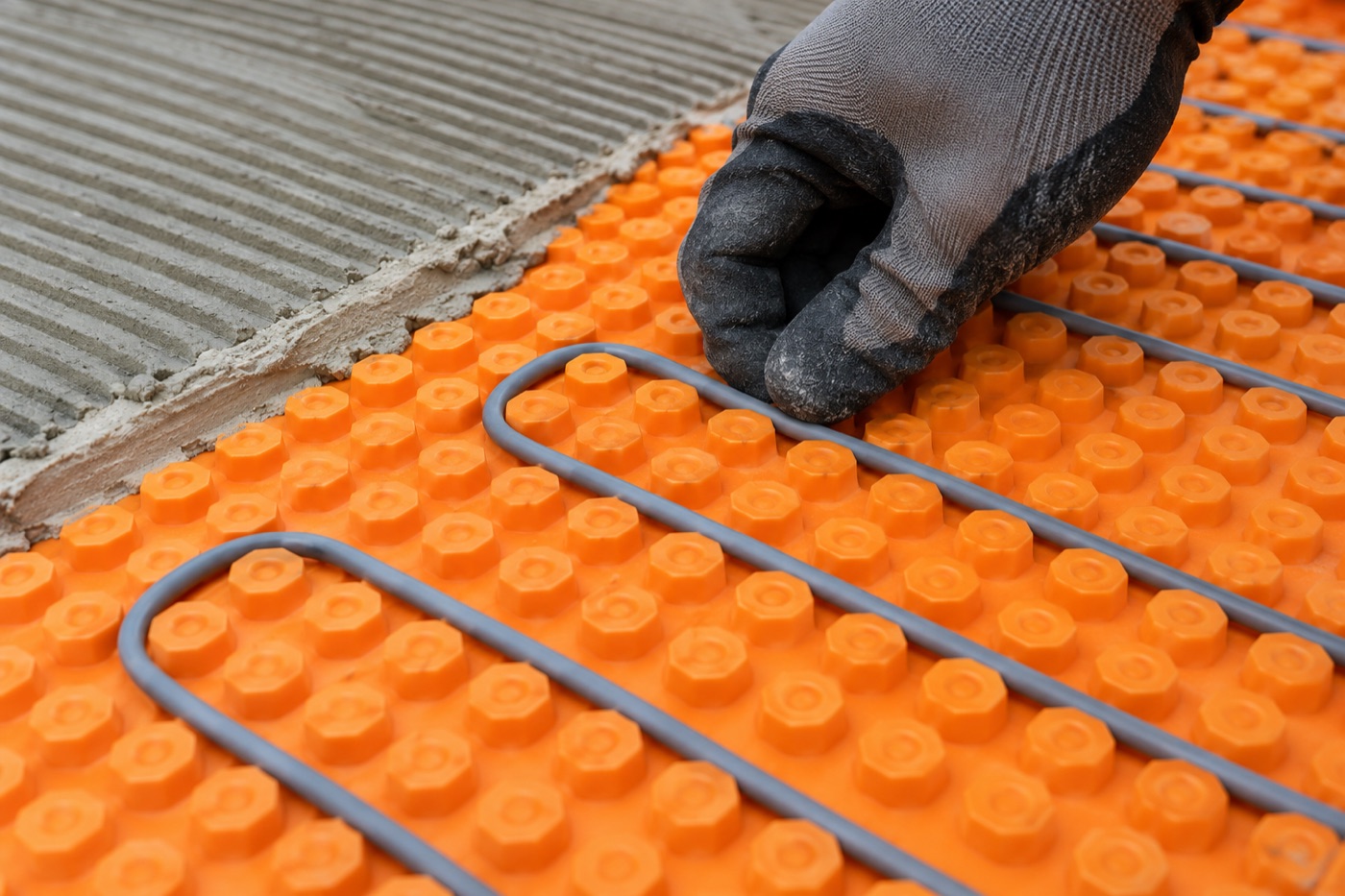Installer pressing electric floor heating cable into the studs of a Schluter DITRA-HEAT uncoupling membrane at standard three-stud spacing